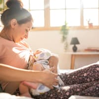 Dauernuckeln: Junge Mutter hält ihr Baby in den Armen zum Stillen und Nuckeln.