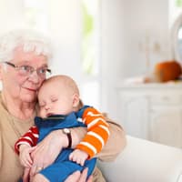Oma hält schlafendes Baby im Arm.