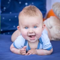 Süßer Babyjunge liegt auf dem Bauch und lächelt in die Kamera. 