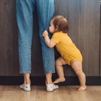 Baby, das sein Gesicht hinter den Beinen seiner Mutter versteckt.