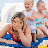 Zwei Mädchen sitzen am Strand auf dem Rücken ihrer Mutter.