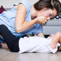 Eine Mutter spielt mit ihrer Tochter und hält sich die Hand vor den Mund.