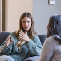 Junge Frau sitzt auf dem Sofa und spricht.