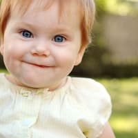 Ein Baby-Mädchen mit roten Haaren lächelt und freut sich über ihren englischen Mädchennamen.