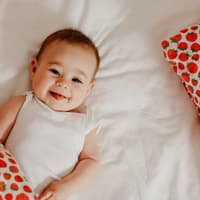 Kleines Baby-Mädchen lacht frech in die Kamera und liegt auf dem Boden.