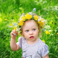 Kleines Mädchen mit Blumenkranz auf dem Haar steht auf einer Wiese.