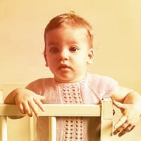Ein Baby-Mädchen in den 60ern steht niedlich im Gitterbett