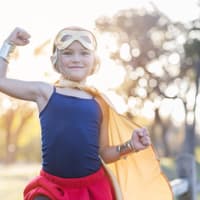 Kleines blondes Mädchen im Superhelden-Kostüm zeigt, wie stark sie ist.