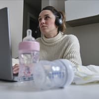 Mutter sitzt mit Milchflaschen und Windeln am Laptop.