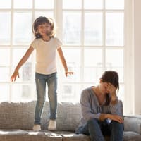 Kind hüpft auf dem Sofa neben erschöpfter Mama.