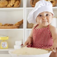 Baby mit Bäckermütze macht Brotteig.