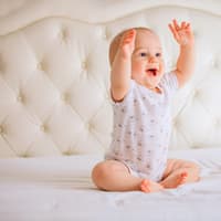 Baby sitzt lachend auf dem Bett.