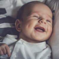 Kleiner Baby-Junge lacht zufrieden und liegt auf dem Bett. 