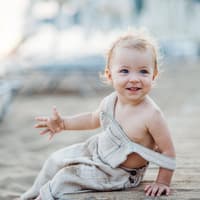 Ein kleines Mädchen sitzt mit Sand an den Händen am Strand.