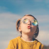 Ein kleines Mädchen schaut mit dicker Sonnenbrille in den Himmel.