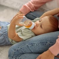 Ein kleiner Baby-Junge trinkt liegend Fencheltee aus einer Nuckelflasche. 