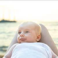 Am Meer: Ein Baby liegt zufrieden auf dem Schoss