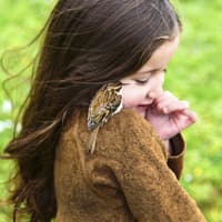 Ein Mädchen mit einem kleinen Vogel auf der Schulter steht auf einer Wiese.