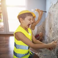 Kind spielt Bauarbeiter und zerstört eine Wand. 
