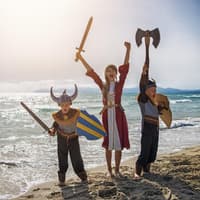 Zwei Jungen und ein Mädchen sind verkleidet als Wikinger am Strand.