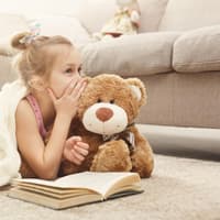 Kleines Mädchen flüstert ihrem Teddy ein Geheimnis ins Ohr.