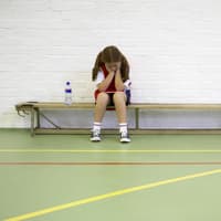 Ein Mädchen sitzt beim Schulsport frustriert auf der Bank. 