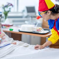 Ein weiblicher Klinik-Clown überrascht ein kleines Mädchen im Krankenhaus.