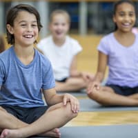 Fröhliche Kinder sitzen in der Schule auf Yogamatten.