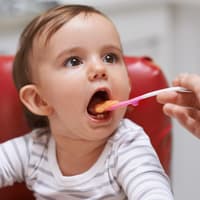 Ein kleines Kind isst einen Löffel Brei aus einem Babygläschen. 