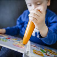 Ein kleiner Junge tippt mit einem orange farbenen Tiptoi-Stift auf ein Tiptoi-Buch.