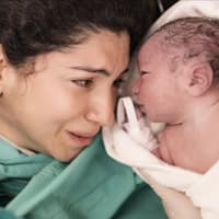 Eine frisch gebackene Mutter weint als sie ihr Baby endlich neben sich liegen hat.