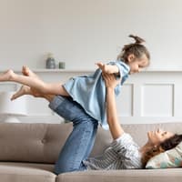 Mutter liegt auf der Couch und hebt ihre Tochter hoch.