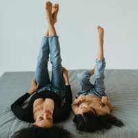 Mutter und Tochter liegen auf dem Rücken und strecken die Beine hoch.