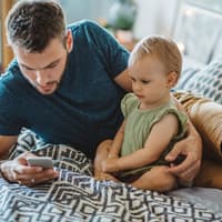 Vater sitzt neben seiner Tochter und guckt aufs Handy