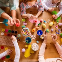 Frauen und Kinder sitzen am Tisch und basteln Ostereier und Osterhasen für Ostern.