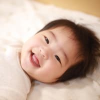 Japanisches Baby liegt lachend im Bett.