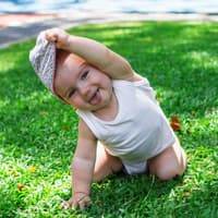 Ein kleines Baby, das sich die Mütze vom Kopf zieht.