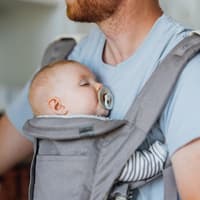 Ein Baby schläft bei Papa in der Trage mit Schnuller