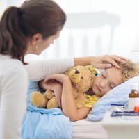 Mutter sitzt neben ihrem kranken Kind am Bett.