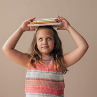 Mädchen balanciert Bücher auf dem Kopf.