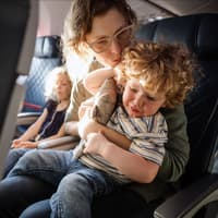 Eine Mutter tröstet ihr Kind im Flugzeug, das Ohrenschmerzen hat. 