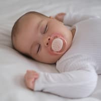 Schlafendes Baby mit Schnuller im Bett