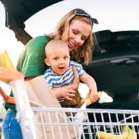Mutter mit Baby und Einkaufswagen am Auto