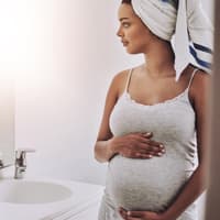 Schwangere Frau steht im Badezimmer.