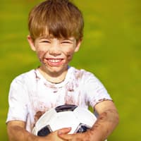Verdrecktes fröhliches Kind mit Fußball.