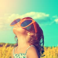 Kind schaut mit riesiger Sonnenbrille in den Himmel.