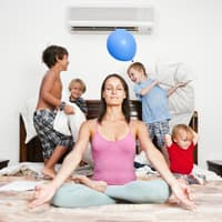 Mutter meditiert auf dem Bett, im Hintergrund toben die Kinder.