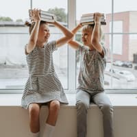 Fröhliche Kinder mit Büchern auf dem Kopf.