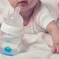Baby mit Wasserflasche im Bett.