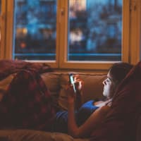 Frau liegt auf dem Sofa und guckt auf ihr Handy.